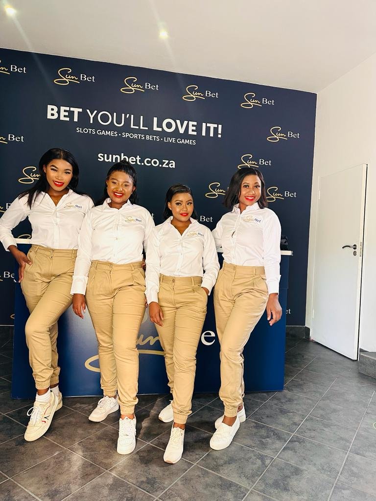 Isilumko-Activate Four women, part of a street-level marketing team, standing in front of a sign that says bet you love it.
