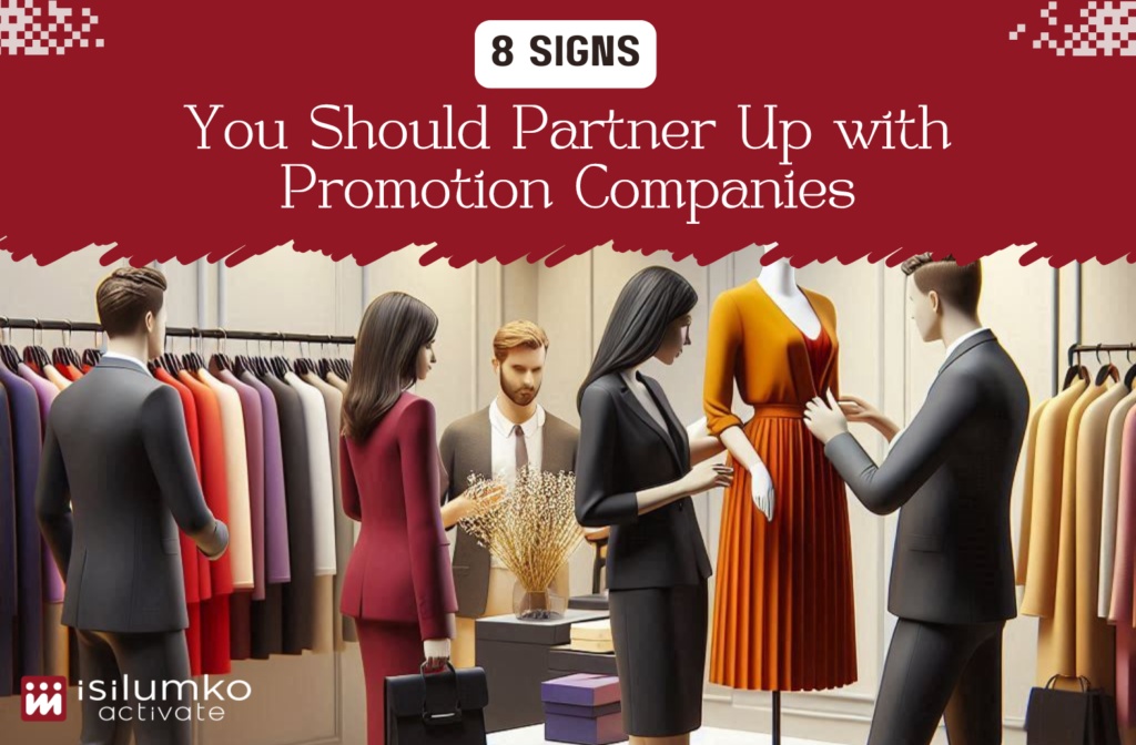Isilumko-Activate Four individuals in a clothing store discuss a dress displayed on a mannequin. The store is neatly arranged with various garments. The image is overlaid with text promoting partnerships with promotion companies.
